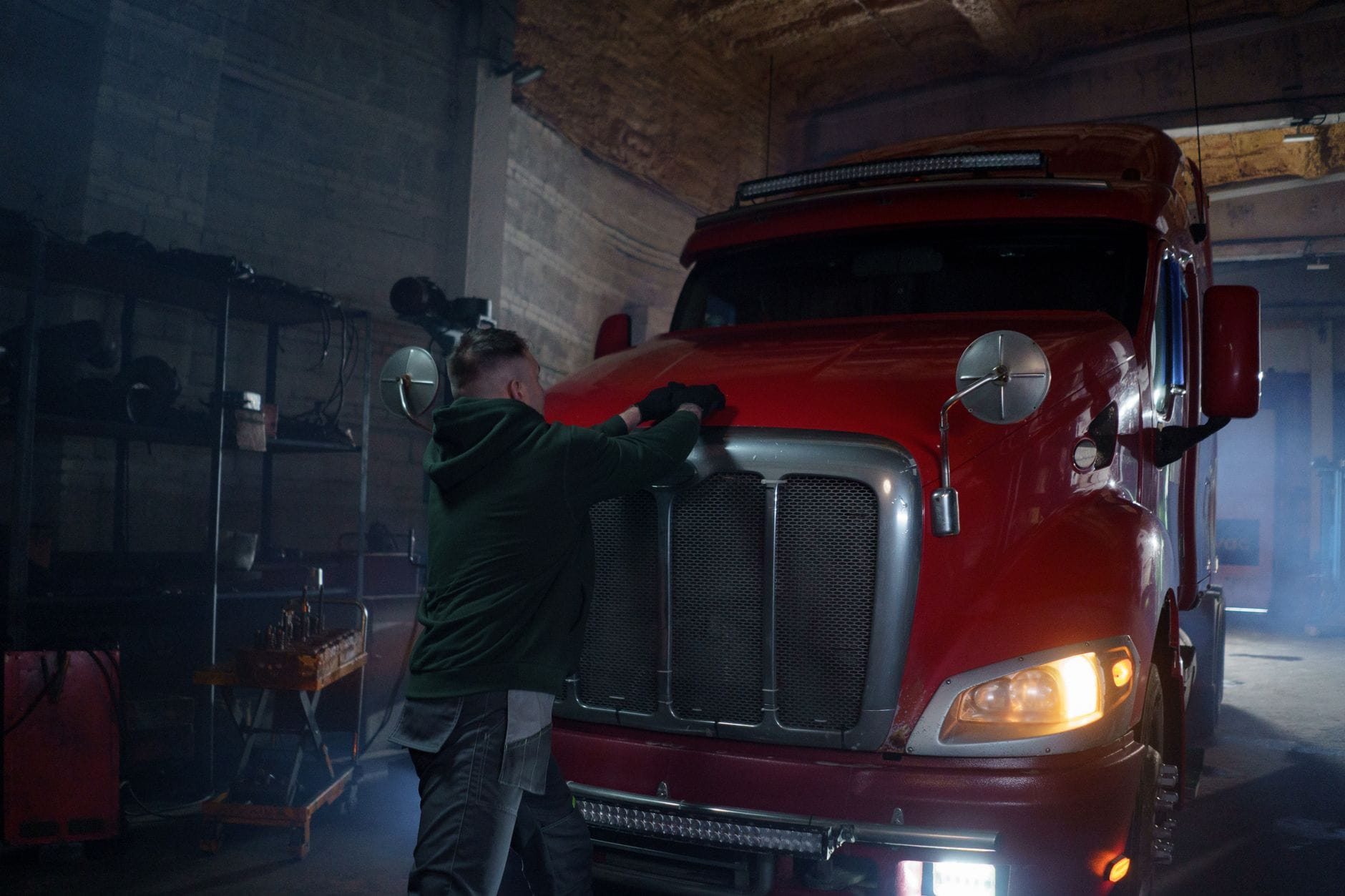 Mechanik w przyciemnionym garażu naprawia czerwony ciągnik siodłowy