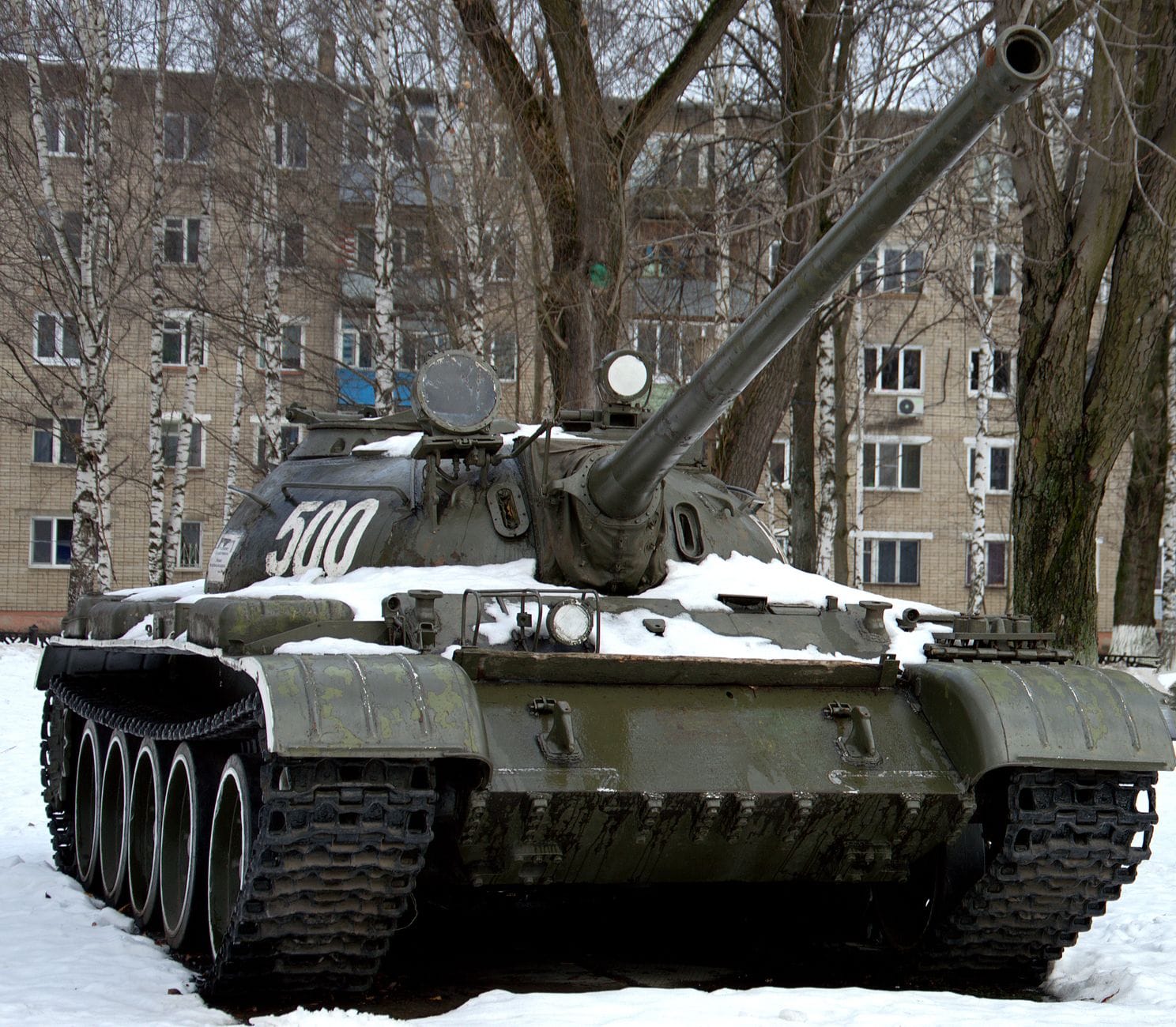 Radziecki czołg T-34/85 zimą, na śniegu wśród drzew i zabudowań