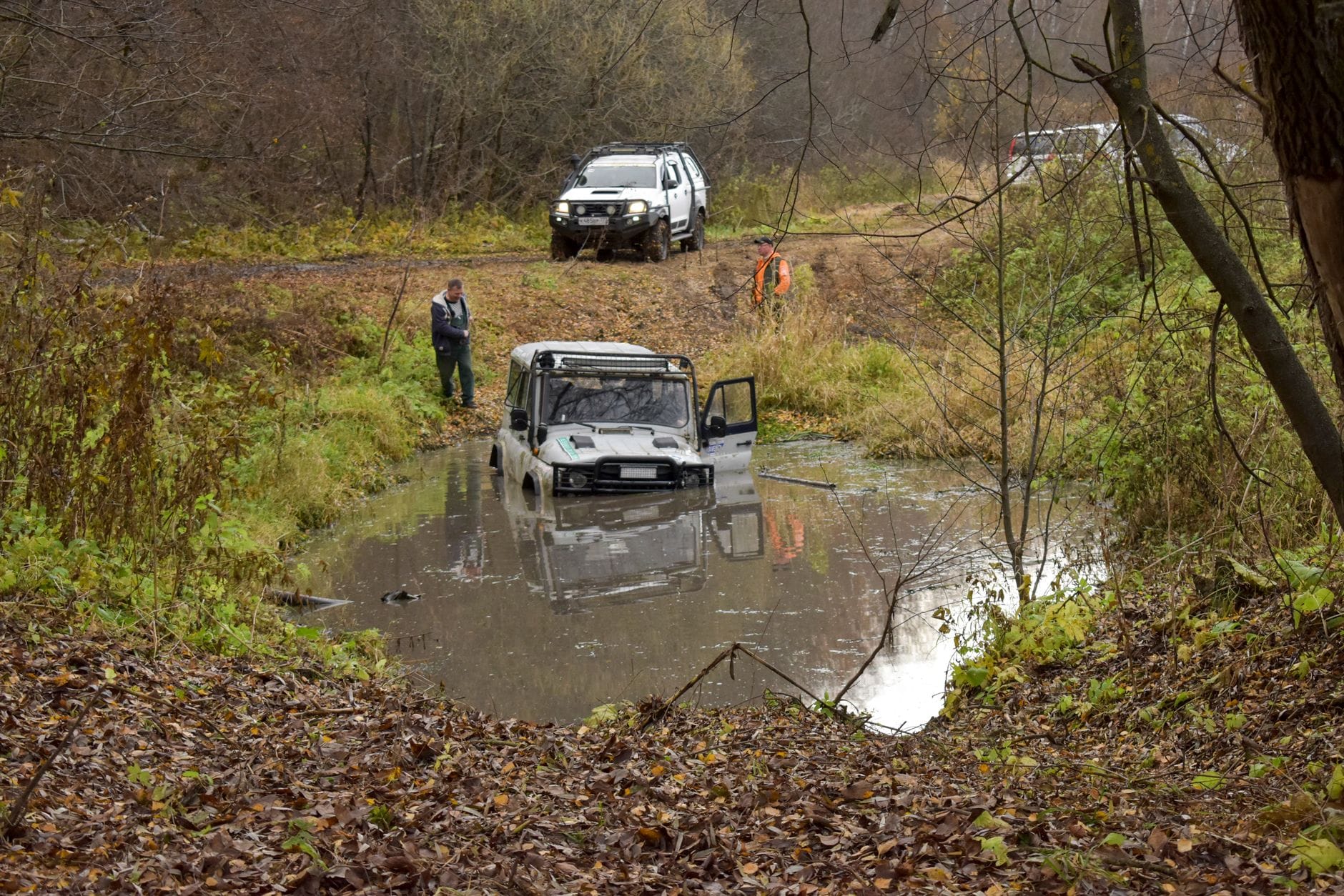 SUV wyciągany z błotnistej kałuży na leśnej drodze, wokół ludzie